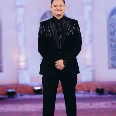 A classic full-length portrait of the groom in a black embellished tuxedo. The styling is sharp and modern, perfect for a grand reception.