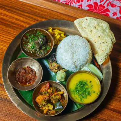 The Chef’s Special Assamese Till Pork Thali is a personal favorite, defined by its rich, nutty black sesame gravy. This top-down view shows the complete meal: tender pork curry, yellow daal, a mixed vegetable side, spicy red chutney, and a mound of steamed rice, all arranged on a traditional brass plate.