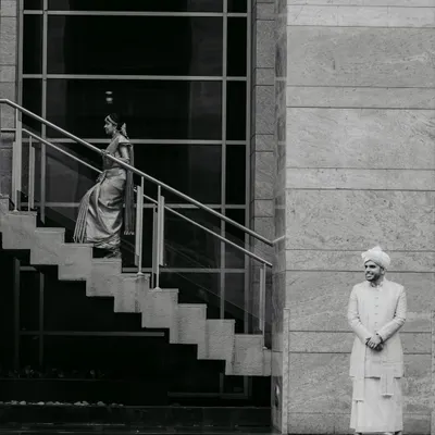 An artistic, black and white shot that plays with architecture and perspective. The groom waits as his bride descends, a moment of anticipation frozen in time.