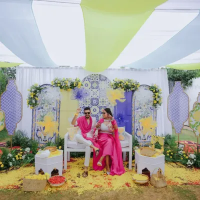 A vibrant Haldi setup featuring a backdrop of blue and yellow tiles, framed by bright pink outfits and a shower of petals. I love creating a playful atmosphere for this fun-filled ceremony.