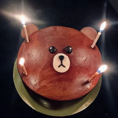 A simple and adorable bear face cake, perfect for any celebration. The lit candles show it's ready for a birthday wish.