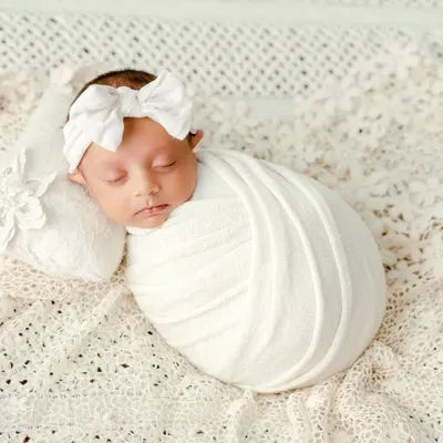 A classic newborn portrait focusing on purity and simplicity. The baby is swaddled snugly in white fabric on a soft, textured blanket, creating a timeless and angelic look.