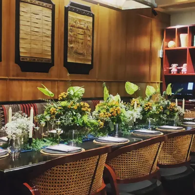 A long table setup for a fine dining experience we curated for the restaurant Burma Burma. The decor features lush, exotic greenery and florals that complement the restaurant's modern Burmese aesthetic.