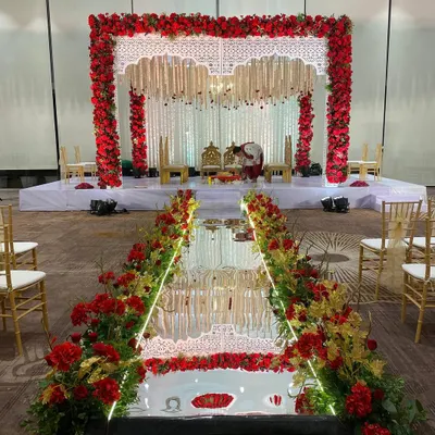 A grand entrance for a classic red and white wedding. The mirrored aisle is lined with red and yellow flowers, leading to a magnificent mandap that promises a beautiful ceremony.