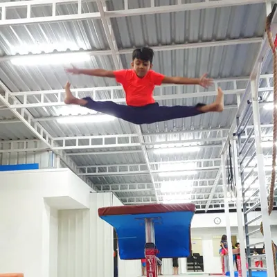 A student achieves a full split jump over the vaulting horse, a dynamic display of power and flexibility.