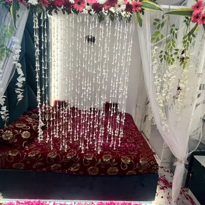 A stunning first night wedding decoration featuring a floral canopy with hanging jasmine strings over a bed covered in rose petals.
