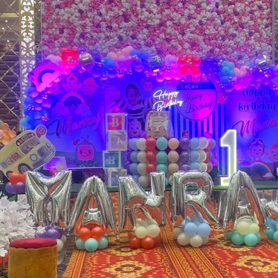 A full view of the spectacular Cocomelon first birthday party setup. The arrangement includes large foil letters for the name, a themed backdrop, balloon arches, and character cutouts, creating an immersive experience for the little one and the guests.
