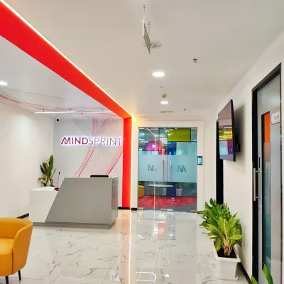 The main reception area for Mindsprint, featuring a clean, modern desk and prominent company branding. The red accent lighting and polished marble floors create a sleek and professional entry point for visitors.