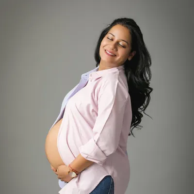 The pure joy and glow of motherhood. This mom-to-be looks so happy and relaxed in a casual open shirt and jeans, showing off her beautiful bump in a simple studio portrait.