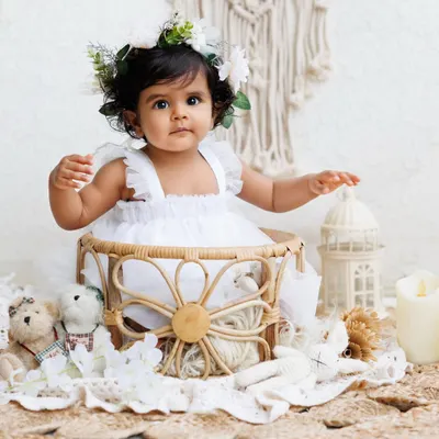 A beautiful baby girl in a white dress and flower crown, sitting in a bohemian-style wicker basket. This theme is simple, elegant, and timeless.