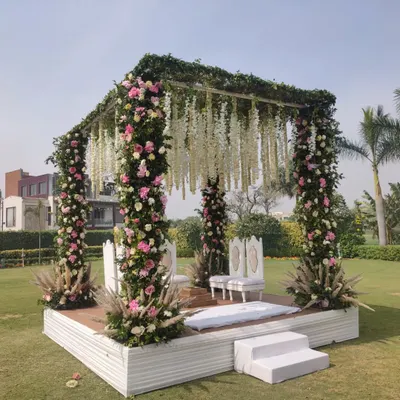 A closer look at a beautiful floral mandap for a daytime wedding. The pillars are densely wrapped with pink and white flowers, and the roof is adorned with hanging white floral strings, creating a lush, garden like feel.