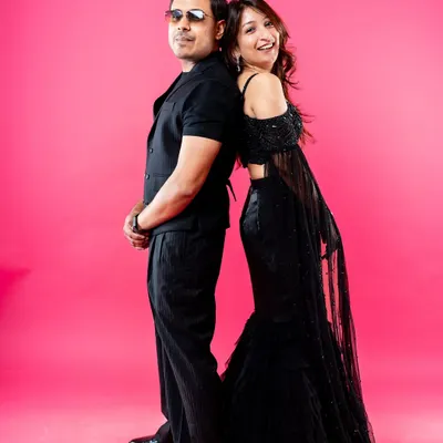 A stylish and fun studio portrait of a couple standing back-to-back. Dressed in black against a vibrant pink background, this shot captures their cool confidence and playful connection, making for a modern pre-wedding photo.