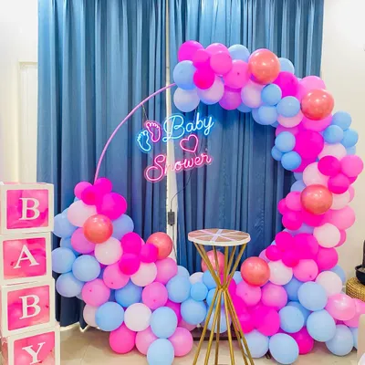 A modern baby shower setup with a circular balloon arch in pink, blue, and white. The custom "Baby Shower" neon sign with a small footprint detail adds a unique and stylish touch to the celebration.