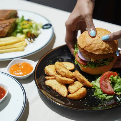 Here is my Ultimate Veg Burger, featuring a crispy patty, fresh lettuce, tomato, and onion in a soft bun. It's served with a side of seasoned potato wedges and dipping sauce.