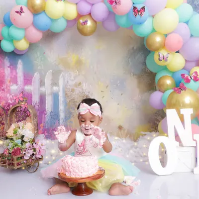 A first birthday cake smash is all about messy fun! This little girl is enjoying her pink cake in a pastel rainbow setup complete with a balloon arch and butterfly details.