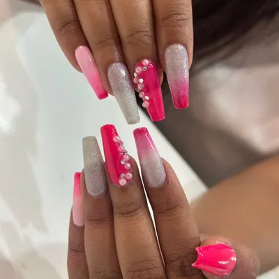 This long coffin nail set is all about vibrant color and sparkle. It features a pink ombre, silver glitter, and a hot pink accent nail with a cascade of pearl embellishments.
