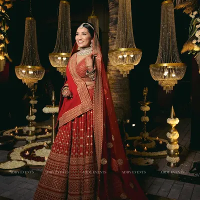 A bride looking like absolute royalty. Dressed in a stunning red lehenga, she is perfectly framed by our opulent decor of grand chandeliers and floral arrangements.