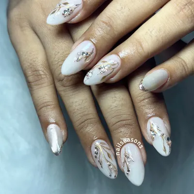 An elegant white manicure with hand-painted gold and silver leafy vines, accented with sparkling rhinestones.