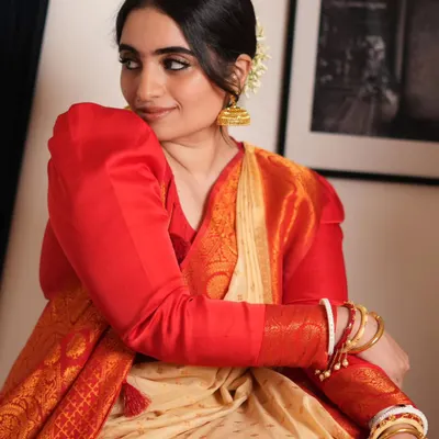 A beautiful moment captured, showcasing the elegance of a traditional Bengali saree. The puffed-sleeve blouse and classic red and cream saree are iconic, and I teach how to drape the fabric to achieve this soft, graceful fall.