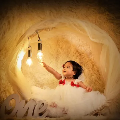 A dreamy first birthday portrait for a little princess. The glowing lights, fluffy clouds, and elegant dress create a magical scene to celebrate her turning one.