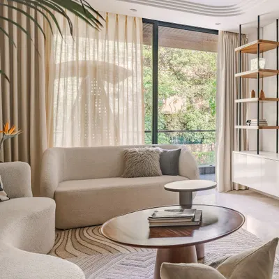 This living room, designed with a Zen-like calm and Wabi-Sabi influences, features curved white sofas that anchor the space. Layered rugs and deep wood coffee tables add texture and warmth, creating a light, airy, and welcoming atmosphere for a young family.
