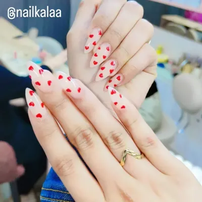 A sweet and romantic design featuring tiny, hand-painted red hearts scattered over a sheer nude base on long stiletto nails.
