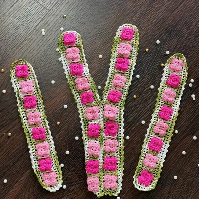 This ready-to-use set includes a V-shaped neckline piece and two matching sleeve cuffs. It features delicate pink crochet flowers arranged on a green base, perfect for embellishing ethnic or casual wear.