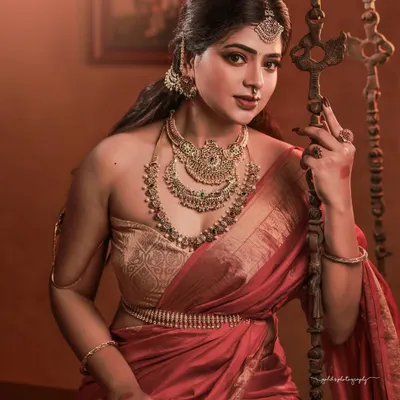 A portrait that feels like a classic painting. The composition, with the bride seated by a traditional swing in a heritage home, combined with the rich red saree and antique gold jewelry, creates a powerful and regal image.