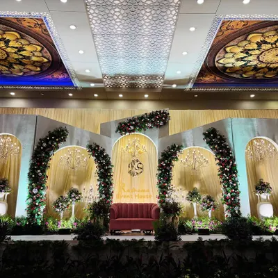 A breathtaking reception stage featuring Roman-style arches, cascading floral arrangements, and elegant chandeliers. The design complements the venue's ornate ceiling, creating a cohesive and luxurious look.