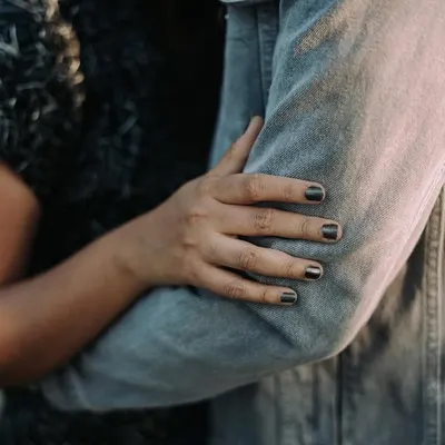 A close-up detail shot of a woman's hand with dark nail polish resting on her partner's denim-clad arm. This photo focuses on the small, intimate gestures of connection.