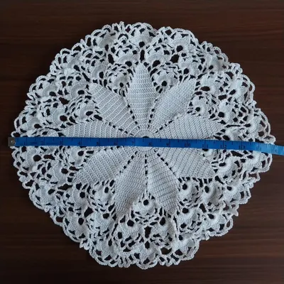 A large, 15-inch white crochet doily with a beautiful star-like pattern. I'm showing the size with a measuring tape. It's perfect as a statement table centerpiece.