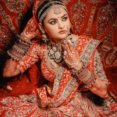 A truly classic bridal portrait. The bride's pose, her stunning red and gold lehenga, and the intricate details of her jewelry are all highlighted to create an image of timeless Indian bridal beauty.