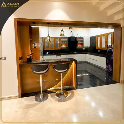 An open-concept kitchen with a stylish breakfast bar and modern stools. The design features a mix of wood and white cabinets, black granite countertops, and elegant pendant lighting.