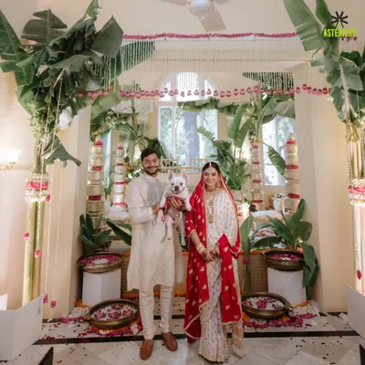 An intimate home wedding, where the couple stands with their furry friend in front of a beautiful, minimalist mandap made with banana leaves and tuberoses.