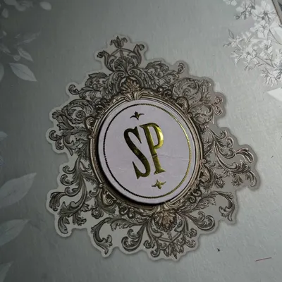 This is what I mean by a signature story. A close-up of a custom 'SP' monogram, crafted with gold foil and surrounded by an intricate, vintage-inspired silver emblem.