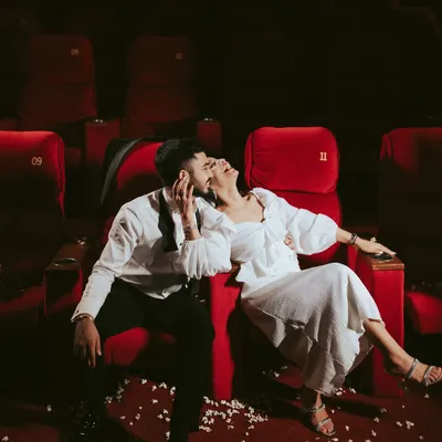 A moment of pure, unscripted joy during a unique pre-wedding shoot in an empty theatre. The dramatic red seats and scattered popcorn set the stage, but their genuine laughter is the real story here, showcasing a love that's playful and real.