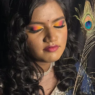 A vibrant Haldi and Mehandi makeup look featuring a stunning sunset eye with shades of orange, yellow, and pink. Paired with soft curls and a peacock feather prop, this look is perfect for pre-wedding festivities.
