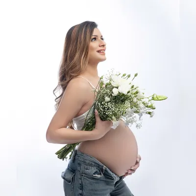 Blooming with joy. A simple, fresh, and modern maternity portrait with a beautiful bouquet of white flowers. The focus is all on that gorgeous baby bump and happy smile.