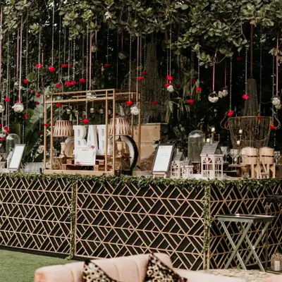 This outdoor bar setup was designed for a chic daytime event. It features a custom bar with a modern geometric pattern, complemented by elegant hanging floral decor and birdcage accents.