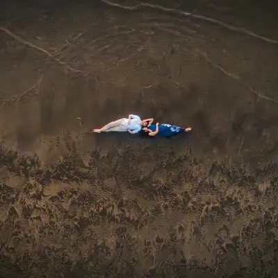 An artistic aerial shot of the couple lying on the wet sand. The patterns left by the waves create a beautiful, textured canvas, turning a simple moment into a piece of art.