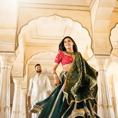 A vibrant shot of a bride in a traditional green bandhani lehenga, her joyful expression captured as she walks through a palace corridor in Jaipur.