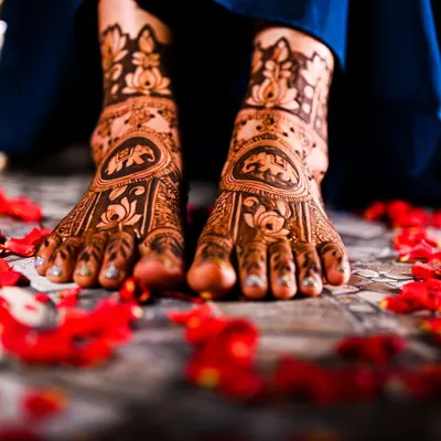 Beautifully captured bridal feet mehendi, adorned with lotus and elephant motifs and surrounded by delicate rose petals.