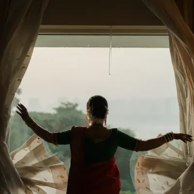 A bride looks out the window, a quiet moment of reflection before her Marathi wedding ceremony begins. The silhouette against the curtains creates a poetic and timeless bridal portrait.