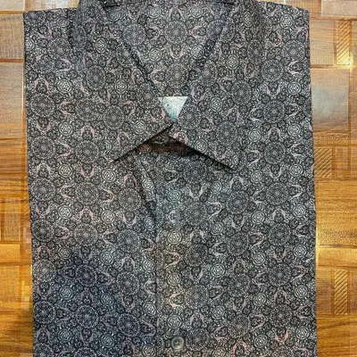 A finished custom shirt made from a fine printed cotton fabric. The shirt is expertly folded to showcase the crisp collar and intricate pattern.