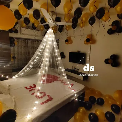 For this romantic room decoration, we installed a delicate canopy draped with fairy lights over the bed. The look was completed with black and gold balloons and a heart shape made from real rose petals.