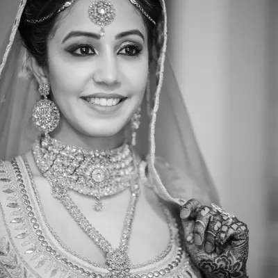 A radiant black and white bridal portrait that captures a genuine smile. Monochrome photography strips away color to focus on emotion, light, and the exquisite detail of the wedding jewelry and henna.