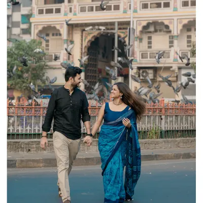 A classic Mumbai pre-wedding shot, capturing the couple walking hand-in-hand as pigeons take flight around them.