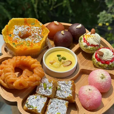 My signature mithai platter offers a beautiful assortment of traditional Indian sweets. It includes Ghewar, Gulab Jamun, Rasgulla, Barfi, Imarti, and Rabri, giving you a taste of all our classic homemade desserts.