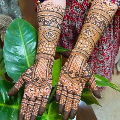 A beautiful, dense bridal mehendi with a mix of geometric checks, floral bands, and delicate details covering the hands and arms.