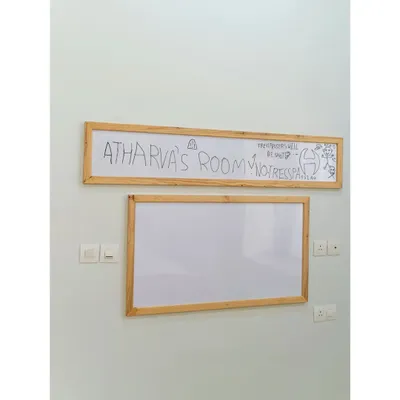 A room truly claimed by its owner! This custom whiteboard with a wooden frame proudly announces "Atharva's Room," serving as a canvas for his creativity and a fun, personal touch to his space-themed bedroom.